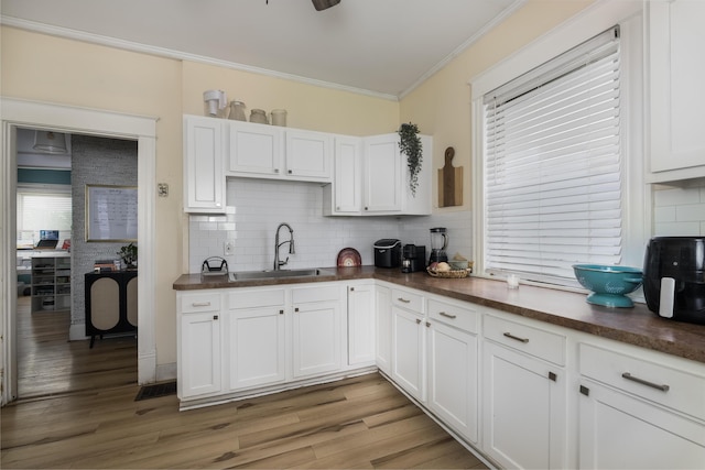 kitchen featuring backsplash, dark countertops, ornamental molding, and a sink