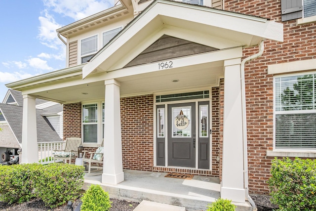 doorway to property with a porch and brick siding