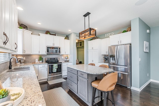 kitchen with appliances with stainless steel finishes, a sink, dark wood-style flooring, tasteful backsplash, and a kitchen island