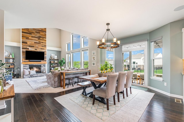 dining space featuring a chandelier, a stone fireplace, dark wood-style flooring, and baseboards