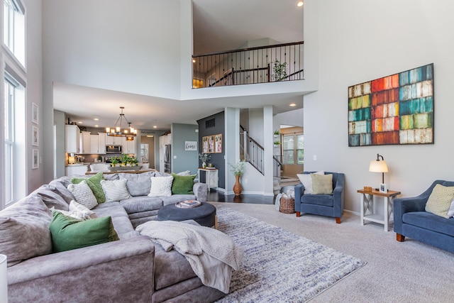 living room featuring a high ceiling, a chandelier, stairway, carpet floors, and baseboards