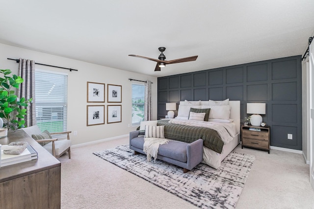bedroom with a decorative wall, light colored carpet, baseboards, and ceiling fan