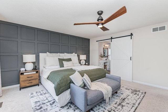 bedroom featuring a barn door, a decorative wall, light colored carpet, ceiling fan, and baseboards