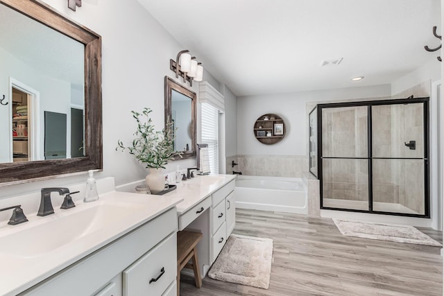 full bath with a shower stall, a garden tub, double vanity, wood finished floors, and recessed lighting