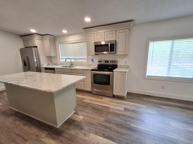 kitchen with wood finished floors, a sink, stainless steel appliances, baseboards, and light stone countertops