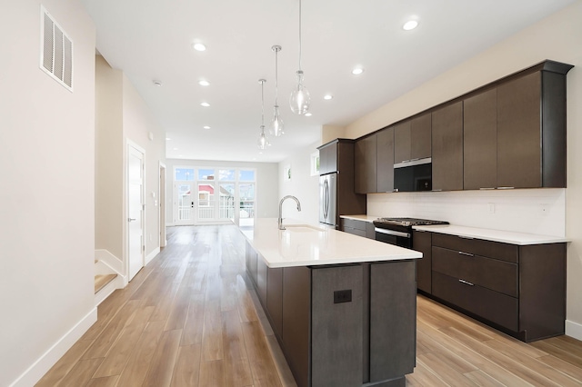 kitchen featuring light wood finished floors, visible vents, a sink, a kitchen island with sink, and appliances with stainless steel finishes