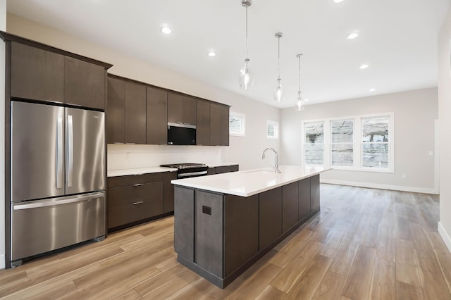 kitchen with dark brown cabinets, a sink, light wood-style floors, light countertops, and appliances with stainless steel finishes