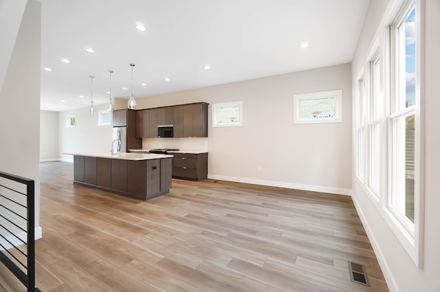 kitchen featuring stainless steel refrigerator, a center island with sink, dark brown cabinetry, light countertops, and baseboards