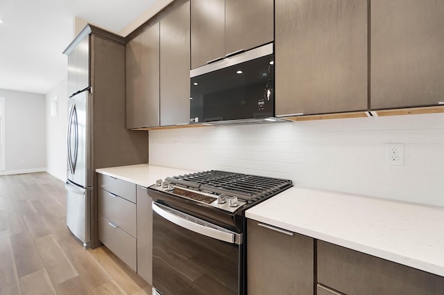 kitchen with light countertops, stainless steel appliances, light wood-style flooring, and backsplash
