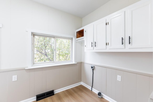 laundry area featuring electric dryer hookup, cabinet space, a wainscoted wall, light wood-type flooring, and visible vents