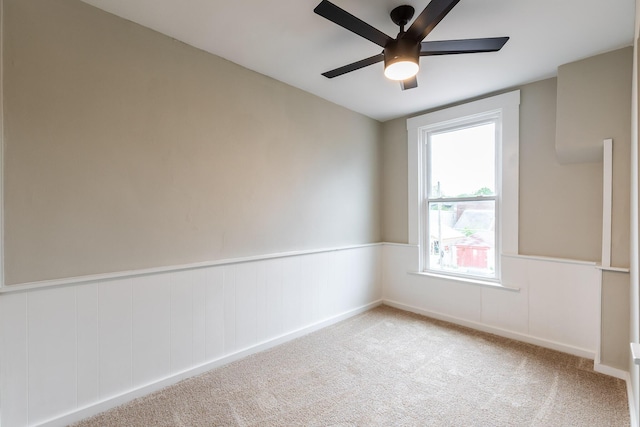 unfurnished room featuring carpet, ceiling fan, and a wainscoted wall
