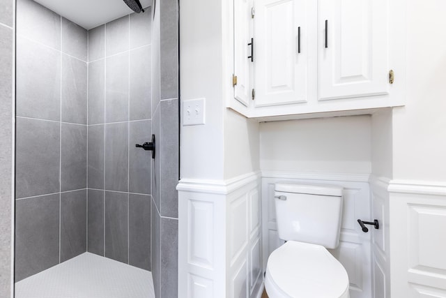 full bathroom with a wainscoted wall, toilet, a decorative wall, and tiled shower