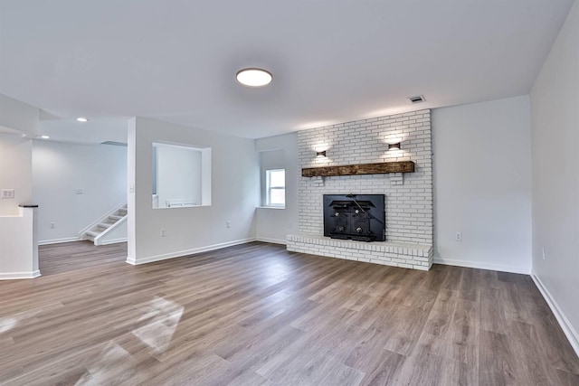 unfurnished living room featuring stairs, wood finished floors, baseboards, a brick fireplace, and recessed lighting