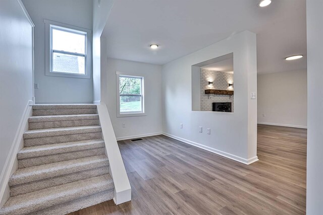 staircase with wood finished floors, baseboards, a brick fireplace, and recessed lighting