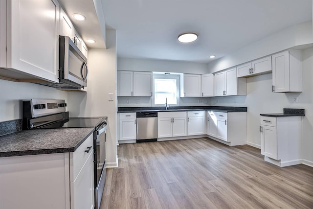 kitchen featuring stainless steel appliances, dark countertops, a sink, white cabinetry, and light wood-style flooring