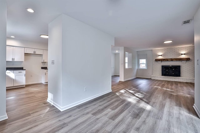 unfurnished living room with light wood finished floors, baseboards, recessed lighting, and a brick fireplace