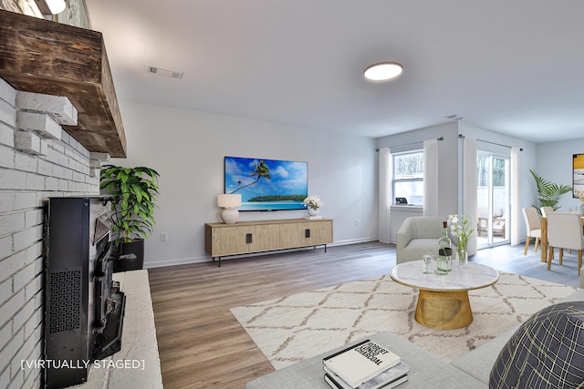 living room featuring a brick fireplace, wood finished floors, and baseboards
