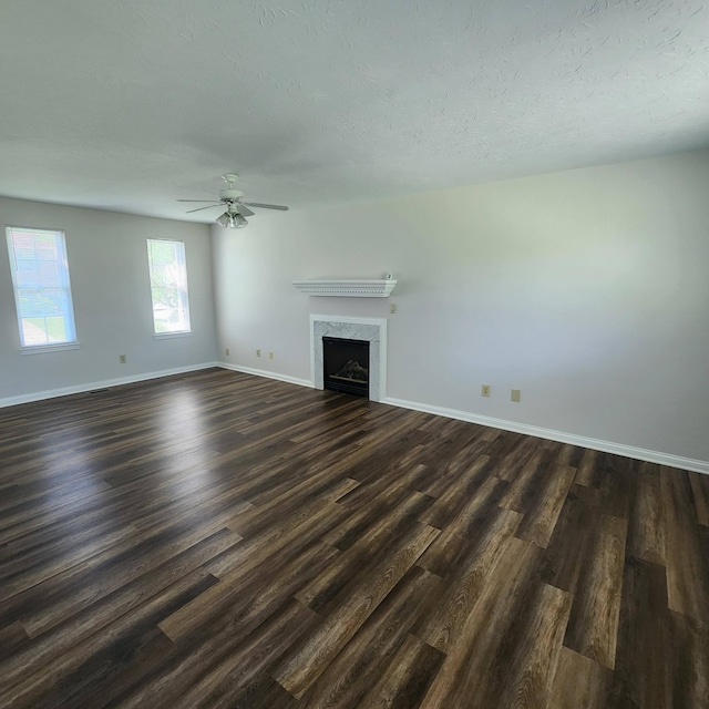 unfurnished living room featuring dark wood-style floors, a fireplace, baseboards, ceiling fan, and a textured ceiling