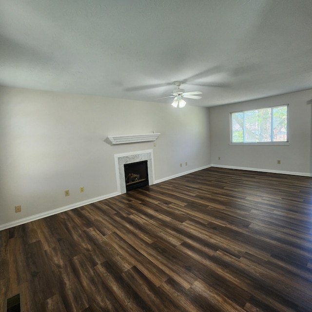 unfurnished living room with a ceiling fan, dark wood finished floors, baseboards, and a fireplace