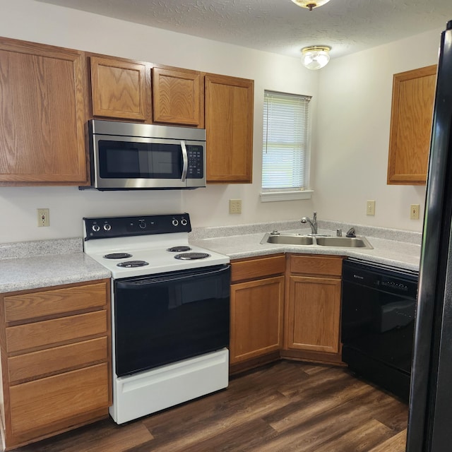 kitchen featuring black appliances, a sink, brown cabinetry, light countertops, and dark wood finished floors