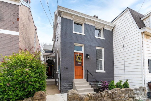 view of front of house featuring brick siding, entry steps, and a chimney