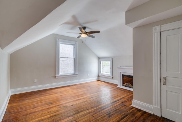 bonus room with ceiling fan, dark wood-type flooring, baseboards, vaulted ceiling, and a glass covered fireplace