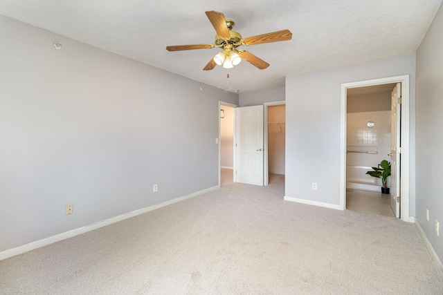 unfurnished bedroom with light colored carpet, a walk in closet, baseboards, a closet, and a ceiling fan