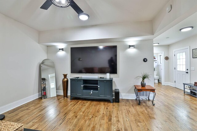 living room featuring ceiling fan, light wood-style flooring, arched walkways, and baseboards