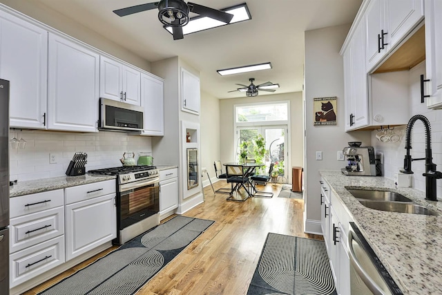 kitchen featuring appliances with stainless steel finishes, ceiling fan, a sink, white cabinetry, and light wood-style flooring