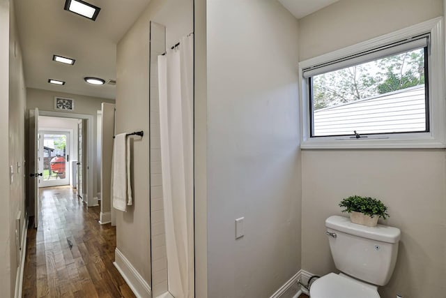 bathroom with toilet, wood finished floors, baseboards, and a shower with curtain