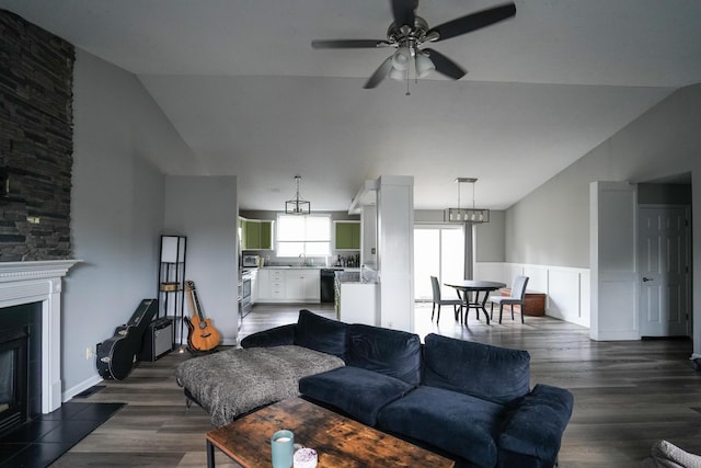 living room with lofted ceiling, a ceiling fan, dark wood-type flooring, a glass covered fireplace, and wainscoting