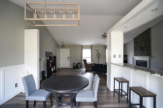 dining area with dark wood-type flooring, a fireplace, ceiling fan, and vaulted ceiling