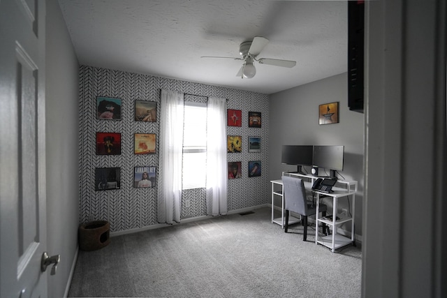 office area featuring wallpapered walls, an accent wall, baseboards, a ceiling fan, and carpet flooring