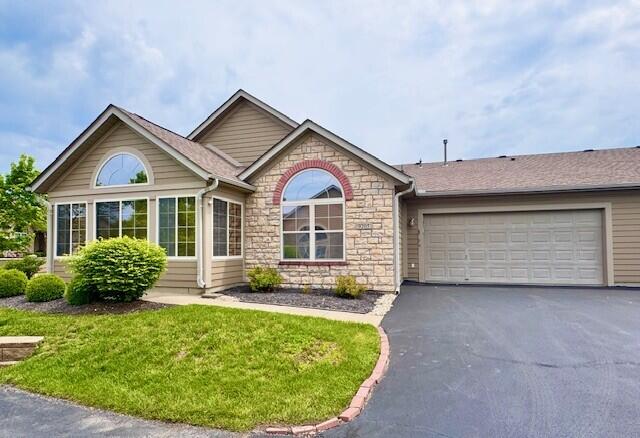ranch-style home featuring stone siding, asphalt driveway, an attached garage, and a front yard
