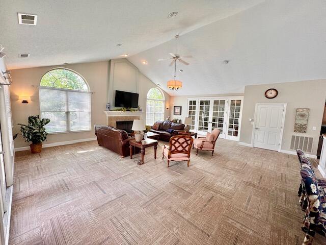 living room with light carpet, a fireplace, baseboards, a ceiling fan, and high vaulted ceiling