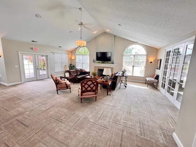 living area with french doors, light carpet, vaulted ceiling, ceiling fan, and a fireplace
