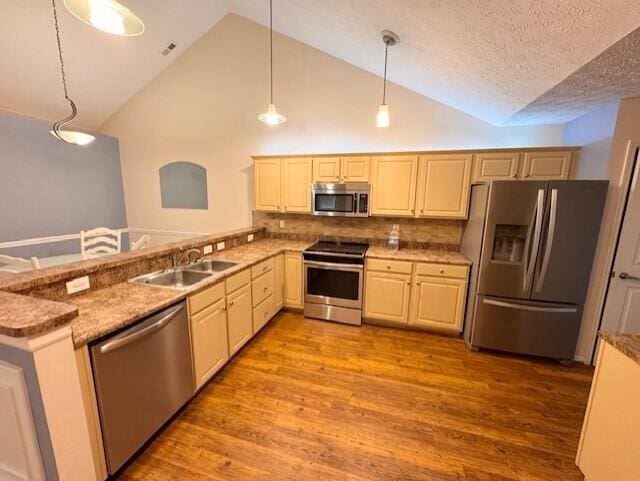 kitchen with appliances with stainless steel finishes, a sink, light wood finished floors, pendant lighting, and backsplash
