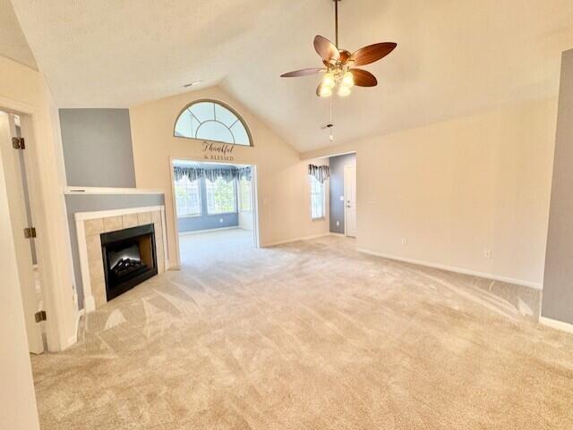 unfurnished living room featuring vaulted ceiling, a ceiling fan, carpet, baseboards, and a tiled fireplace
