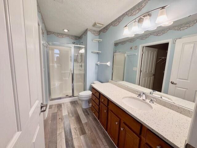 bathroom with a textured ceiling, wood finished floors, a stall shower, vanity, and toilet