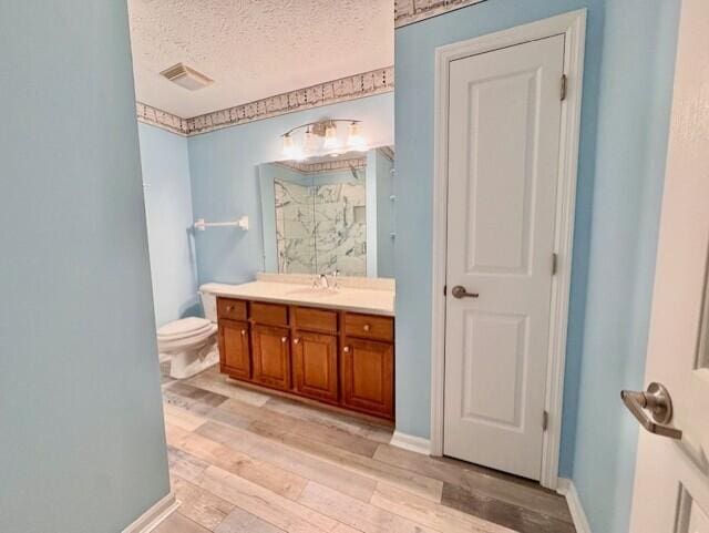 full bathroom featuring wood finished floors, vanity, toilet, a textured ceiling, and a shower