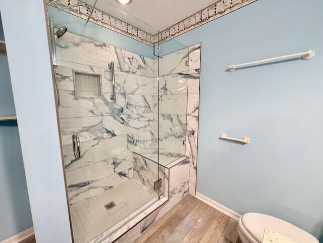 full bathroom with a marble finish shower, toilet, wood finished floors, and baseboards