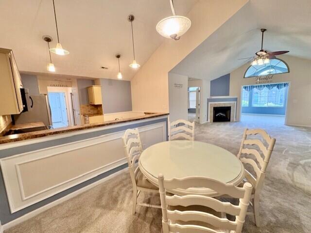 dining room with light carpet, lofted ceiling, a fireplace, and ceiling fan