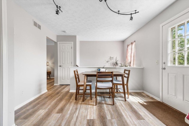 dining space featuring track lighting, wood finished floors, a textured ceiling, and baseboards