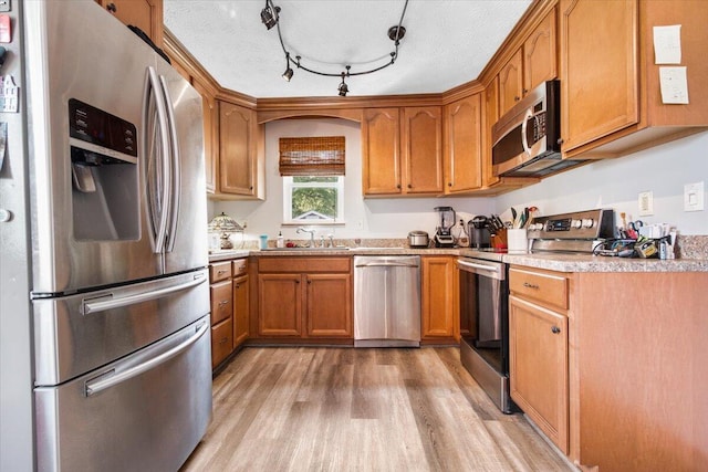 kitchen with appliances with stainless steel finishes, light wood-style flooring, a sink, light countertops, and brown cabinetry