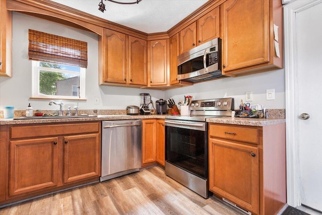 kitchen featuring stainless steel appliances, a sink, light wood-style flooring, brown cabinetry, and light countertops