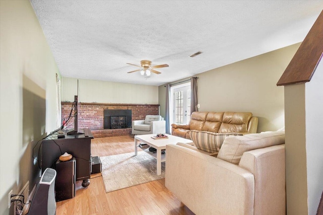 living room with light wood-style floors, a ceiling fan, a textured ceiling, and a wood stove
