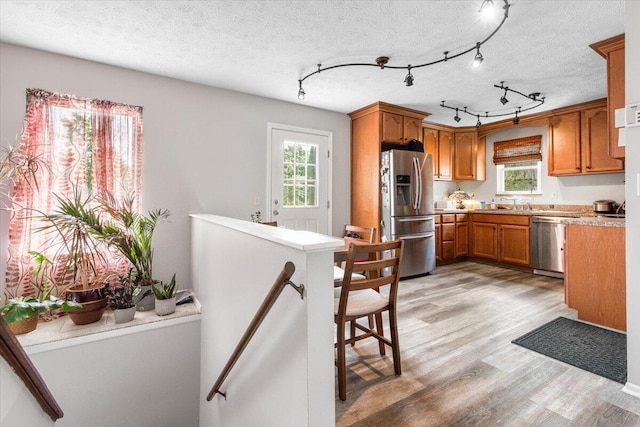 kitchen with appliances with stainless steel finishes, light wood-type flooring, brown cabinets, and healthy amount of natural light