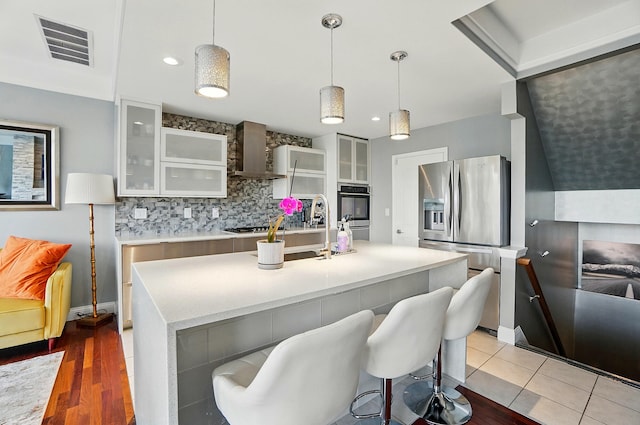 516 Western Ave, Covington, KY 41011 - kitchen featuring wall chimney exhaust hood, stainless steel appliances, tasteful backsplash, an island with sink, and glass insert cabinets
