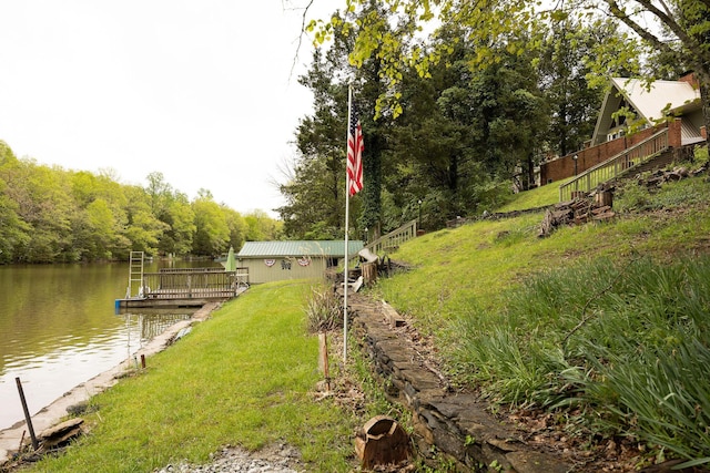 view of grassy yard with a water view, a dock, and a view of trees