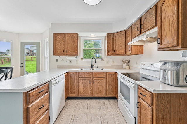 kitchen with white appliances, under cabinet range hood, a sink, a peninsula, and light countertops